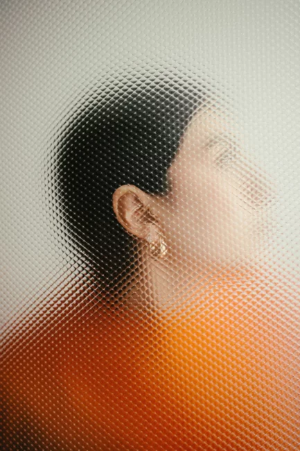Person in orange sweater behind tinted glass.
